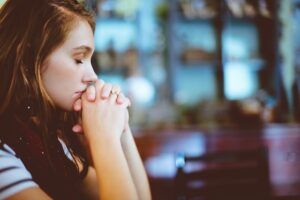 woman-sitting-with-hands-folded-together-in-front-of-her-face