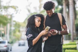man and women standing in a park looking at their phones together